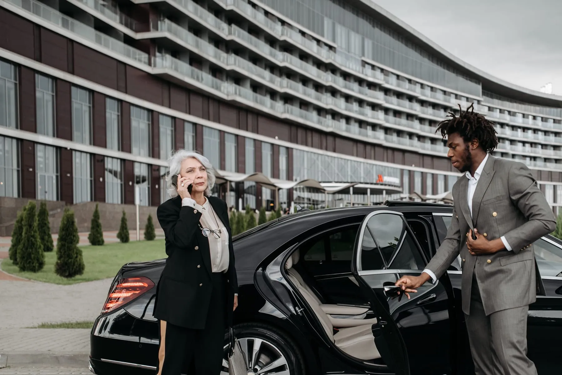 A businesswoman on the phone beside a car door held open by her chauffeur — Chauffeur Service Frankfurt — Private Driver & Business Cars