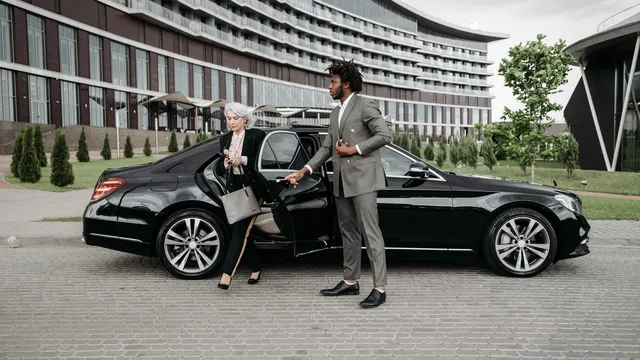A chauffeur holding the rear door of a black saloon at a hotel entrance — Limousine Service Essen – Düsseldorf Airport