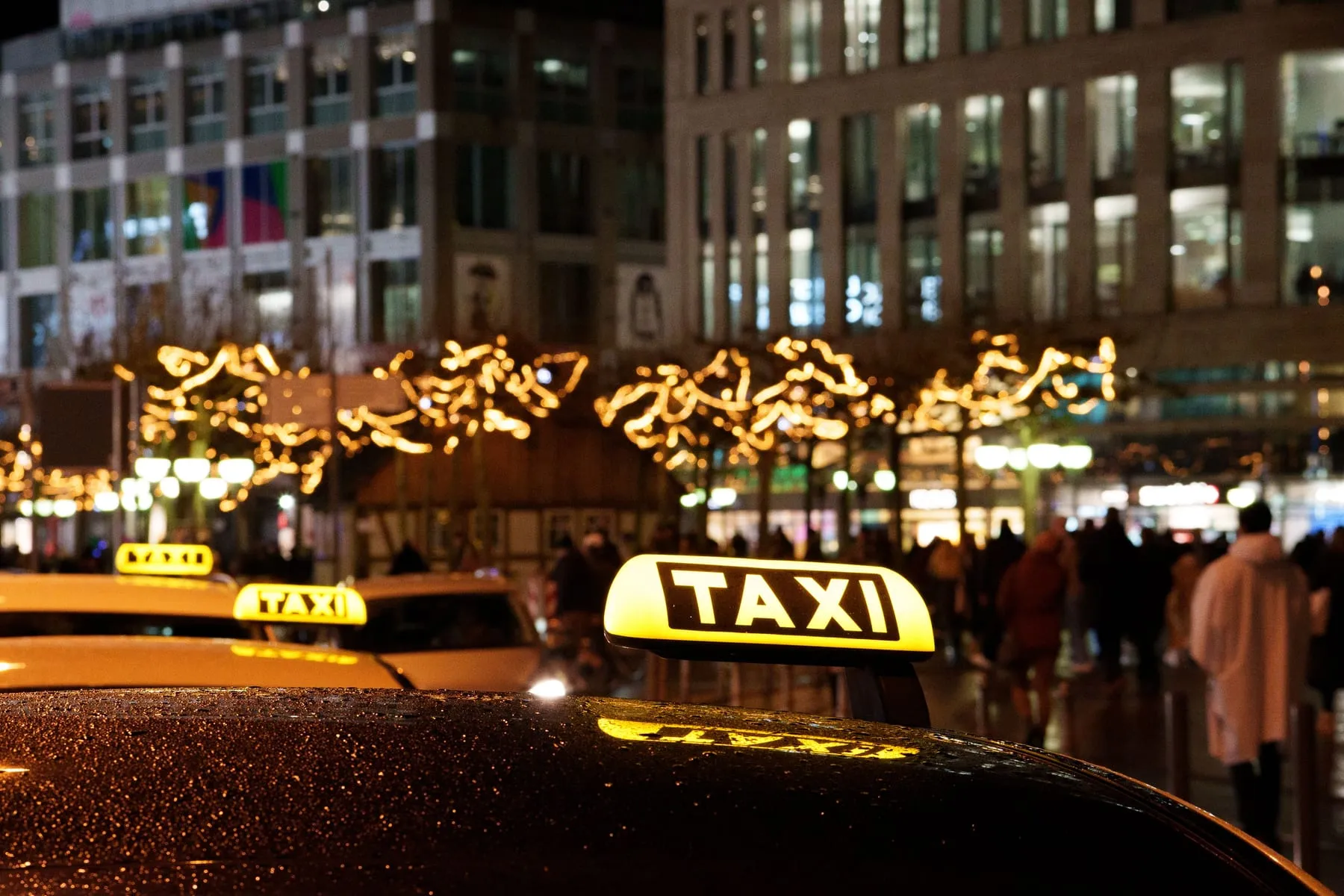 Illuminated German taxi roof signs on a wet city street at night — Taxi to Frankfurt Airport at a Fixed Fare